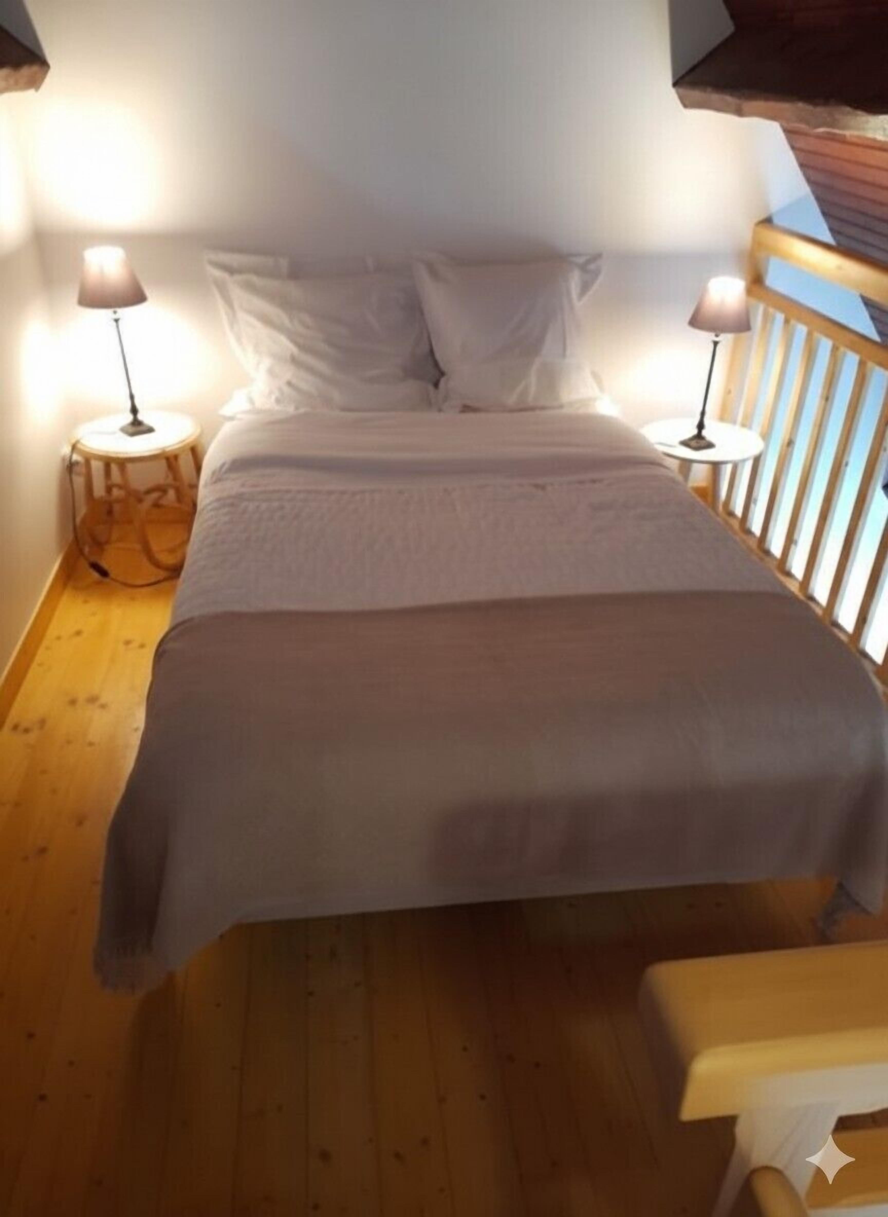A bed with white linens, two bedside lamps, and a wooden floor.