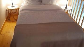 A bed with white linens, two bedside lamps, and a wooden floor.
