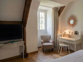 Un dormitorio con televisión, escritorio, silla, cama y ventana con cortinas.