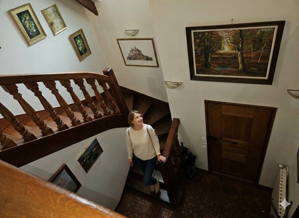 A staircase with wooden railings, a person descending, and framed artwork on the walls.