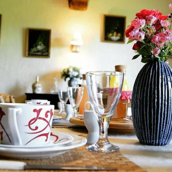 A dining table with white plates and clear glassware, a blue vase with flowers, and framed artwork on the wall. - Bed and Breakfast Saultchevreuil (Villedieu-les-Poêles-Rouffigny)