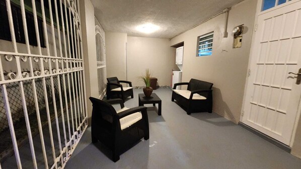 A narrow hallway with two black chairs and a small table, a white door on the right, and a barred gate on the left. - Puerto Rico: 5-Minute Airport / Parking / Carolina, San Juan. (Carolina)