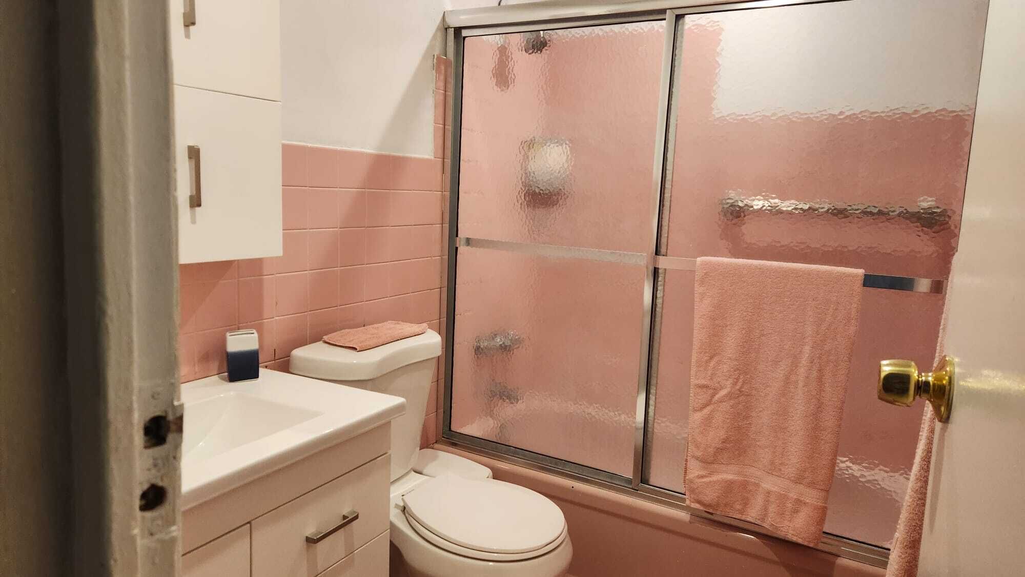 A bathroom with a glass shower enclosure, a toilet, a sink, and a towel hanging on the door.