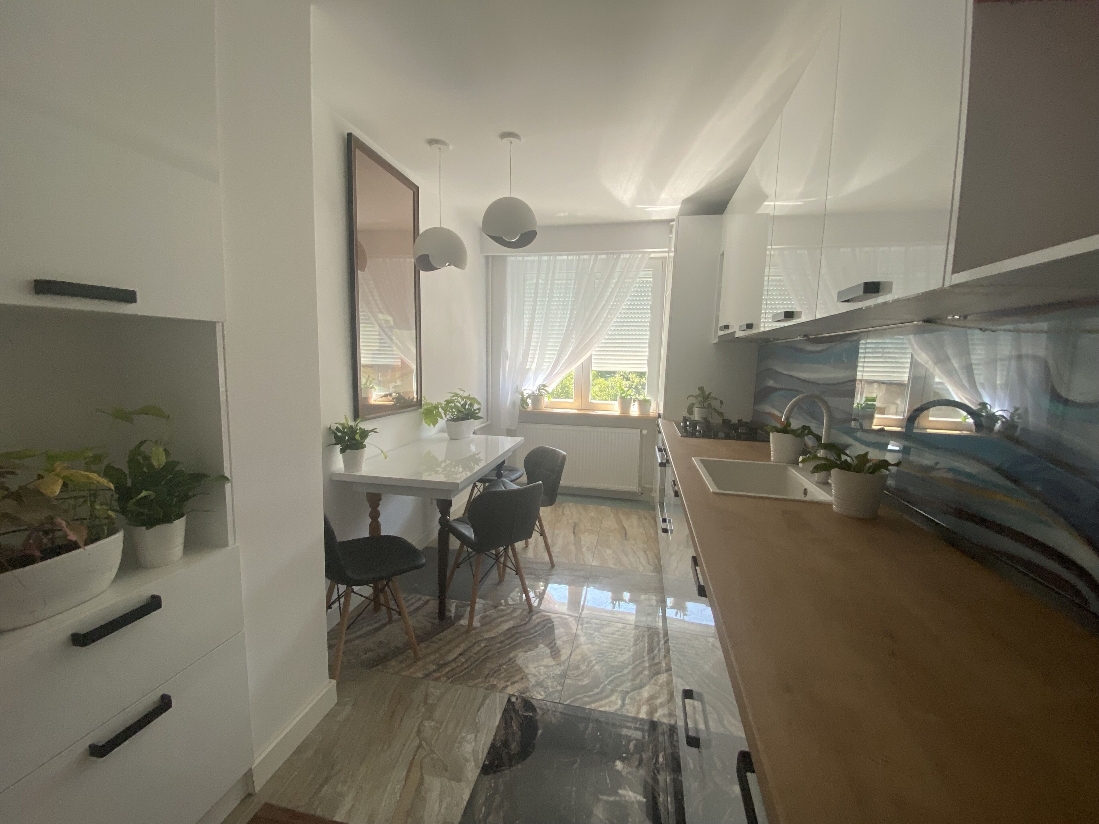 A modern kitchen with white cabinets, a marble countertop, and a dining area with a white table and chairs.