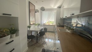 Et moderne køkken med hvide skabe, en marmor bordplade, samt et spiseområde med et hvidt bord og stole.