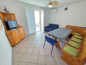 En kompakt opholdsstue med spisebord, blå stole, sofa og fjernsyn på et træskab.