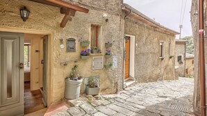 A narrow cobblestone street with stone buildings, wooden doors, and flower boxes. - Appartamenti Anguria Toscana One-bedroom (Sinalunga)