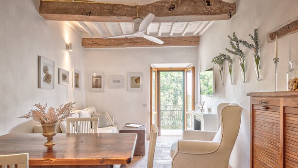 A dining area with a wooden table, chairs, and a vase of dried flowers. There are framed pictures on the wall and a ceiling fan. - Appartamenti Anguria Toscana One-bedroom (Sinalunga)