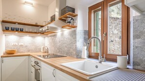A modern kitchen with white cabinets, a wooden countertop, a built-in oven, a sink, and a window with a stone wall view. - Appartamenti Anguria Toscana Two-bedroom (Sinalunga)