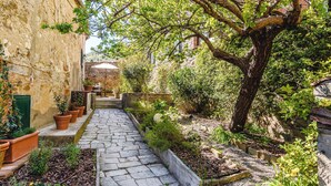 A stone pathway leading through a garden with potted plants and a large tree. - Appartamenti Anguria Toscana Two-bedroom (Sinalunga)
