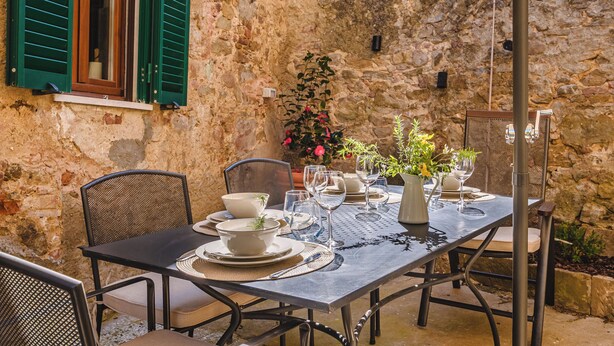 A stone-walled outdoor dining area with a table set for two, featuring metal chairs and a metal table. - Appartamenti Anguria Toscana Two-bedroom (Sinalunga)