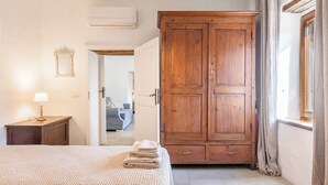 A bedroom with a large wooden wardrobe, a bed with a beige blanket, a bedside table with a lamp, and a mirror on the wall. - Appartamenti Anguria Toscana Two-bedroom (Sinalunga)
