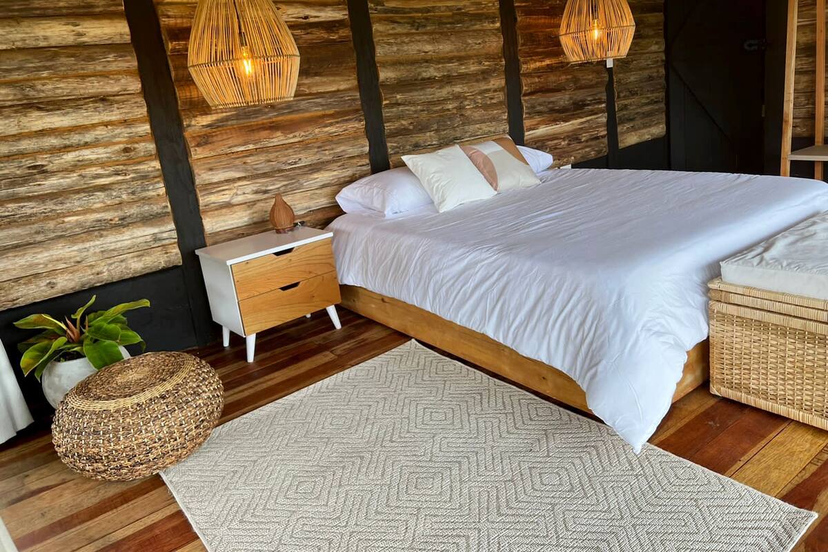 A bedroom with a wooden wall, a bed with white bedding, two bedside tables, and two hanging light fixtures.