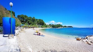A beach with clear blue water, a few people sunbathing, and a blue lamp post. - Apartment With Large Garden in the Heart of Split (Split)