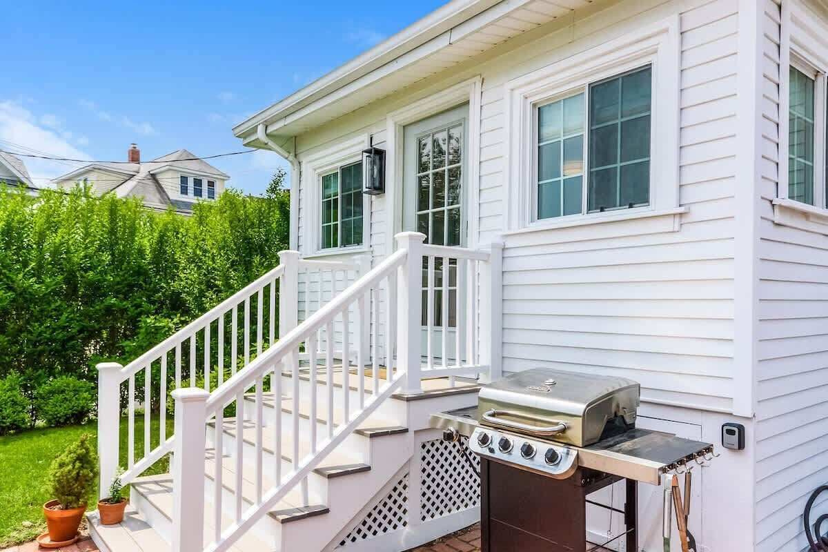 A white house with a porch, a grill, and a staircase.