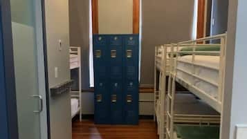 A narrow hallway with wooden flooring, bunk beds on the right, and blue lockers in the center.