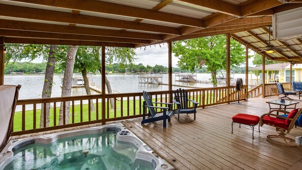 Um deck de madeira com banheira de hidromassagem, cadeiras e vista para um lago.