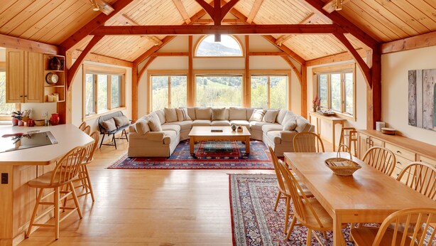 Un vaste espace de vie doté d’un haut plafond en bois, d’un grand canapé, d’une table à manger et d’un coin cuisine avec des meubles en bois et une grande fenêtre.