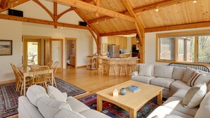 Un vaste espace de vie doté d’un haut plafond en bois, d’une table à manger avec des chaises, d’un canapé et d’une cuisine à l’arrière-plan.