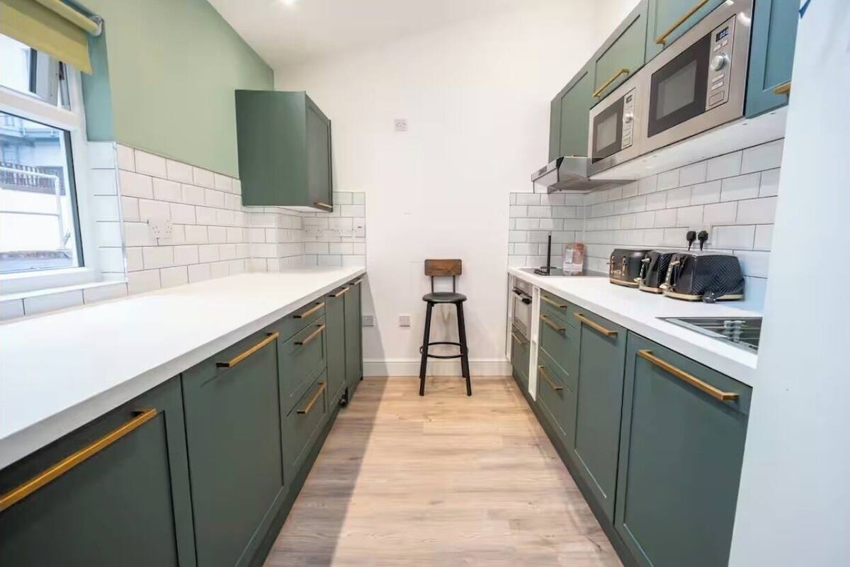 A narrow kitchen with green cabinets, white countertops, and a wooden floor.