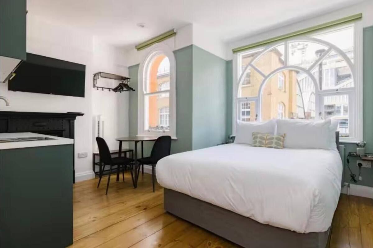 A modern bedroom with a large bed, a small desk, and a window with arched frames.