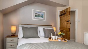 Une chambre à coucher avec un lit, des tables de chevet, un plateau contenant des éléments de petit-déjeuner, un tableau encadré au mur et une porte en bois.