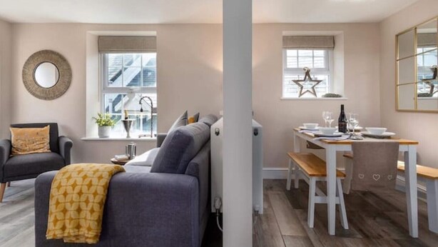 Un salon moderne avec un canapé gris, un miroir rond et un coin repas comprenant une table et des chaises en bois.
