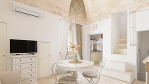 A modern living room with a TV, white furniture, a dining table, and a kitchen in the background. - In Alto Mare by Wonderful Italy (Ostuni)