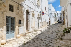 Una estrecha calle adoquinada flanqueada por edificios blancos con puertas en arco y ventanas con rejas.