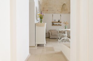 Cocina moderna con armarios blancos, comedor con una silla y mesa blancos, y una lámpara colgante.