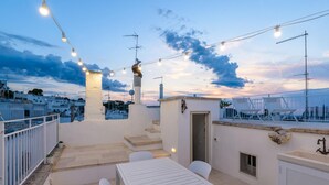 A rooftop terrace with a table and chairs, string lights, and a view of the cityscape. - In Alto Mare by Wonderful Italy (Ostuni)