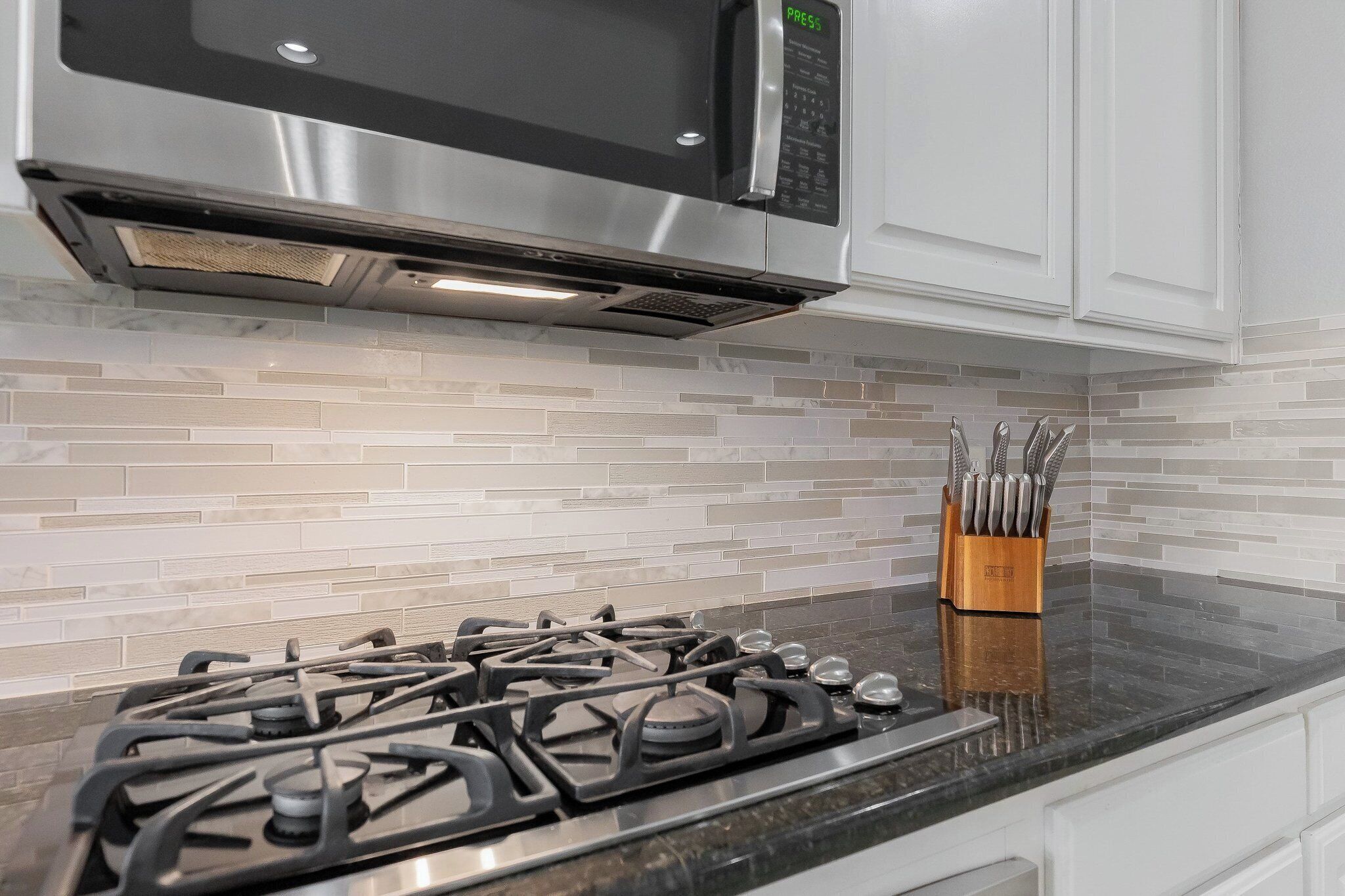 A kitchen with a gas stove, a stainless steel microwave, and a tiled backsplash.