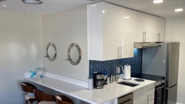 A modern kitchen with a white countertop, stainless steel appliances, and a blue backsplash. - The Turtle Nest 6 in Fort Myers Beach (Fort Myers Beach)