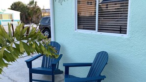 A building with a light blue exterior, a window with horizontal blinds, and two blue Adirondack chairs outside. - The Turtle Nest 6 in Fort Myers Beach (Fort Myers Beach)