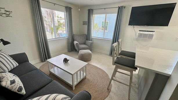 Un salon moderne avec un canapé, une table basse, un fauteuil à motifs et un téléviseur fixé au mur.