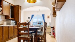 A kitchen with wooden cabinets, a dining table set for four, and a view through an arched window. - Seafront apartment in Gozo, Marsalforn (Zebbug)