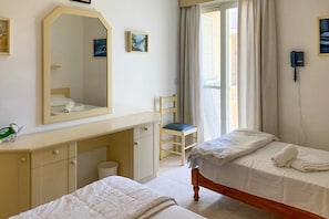 A hotel room with two beds, a desk, a chair, a mirror, a phone, and a window with curtains. - Seafront apartment in Gozo, Marsalforn (Zebbug)