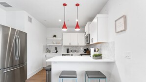 A modern kitchen with white cabinets, a stainless steel refrigerator, a central island with stools, and red pendant lights. - East Downtown 3BR Condo Free Parking Sleeps 7 (Austin)