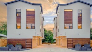 A modern building with two identical structures, each featuring a large window, a wooden panel design at the base, and a flat roof. - East Downtown 3BR Condo Free Parking Sleeps 7 (Austin)
