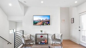 A modern living room with a cityscape painting, a coffee table, two armchairs, and a bookshelf. - East Downtown 3BR Condo Free Parking Sleeps 7 (Austin)