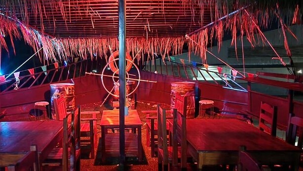 An indoor dining area with wooden tables and chairs, a central pole, and red lighting. - VT SKY SHIP HOTEL (Vientiane)