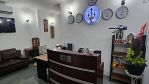 A reception area with a wooden reception desk, multiple wall clocks, a mounted television, and a potted plant. - VT SKY SHIP HOTEL (Vientiane)