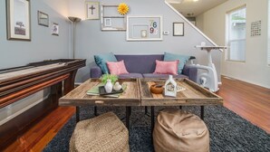 A living room with a piano, a sofa with cushions, a coffee table with decorative items, and a staircase in the background. - Book NOW for Summer Fun! - Perfect for family! - Fully Loaded! - Fire Pit! (Portland)