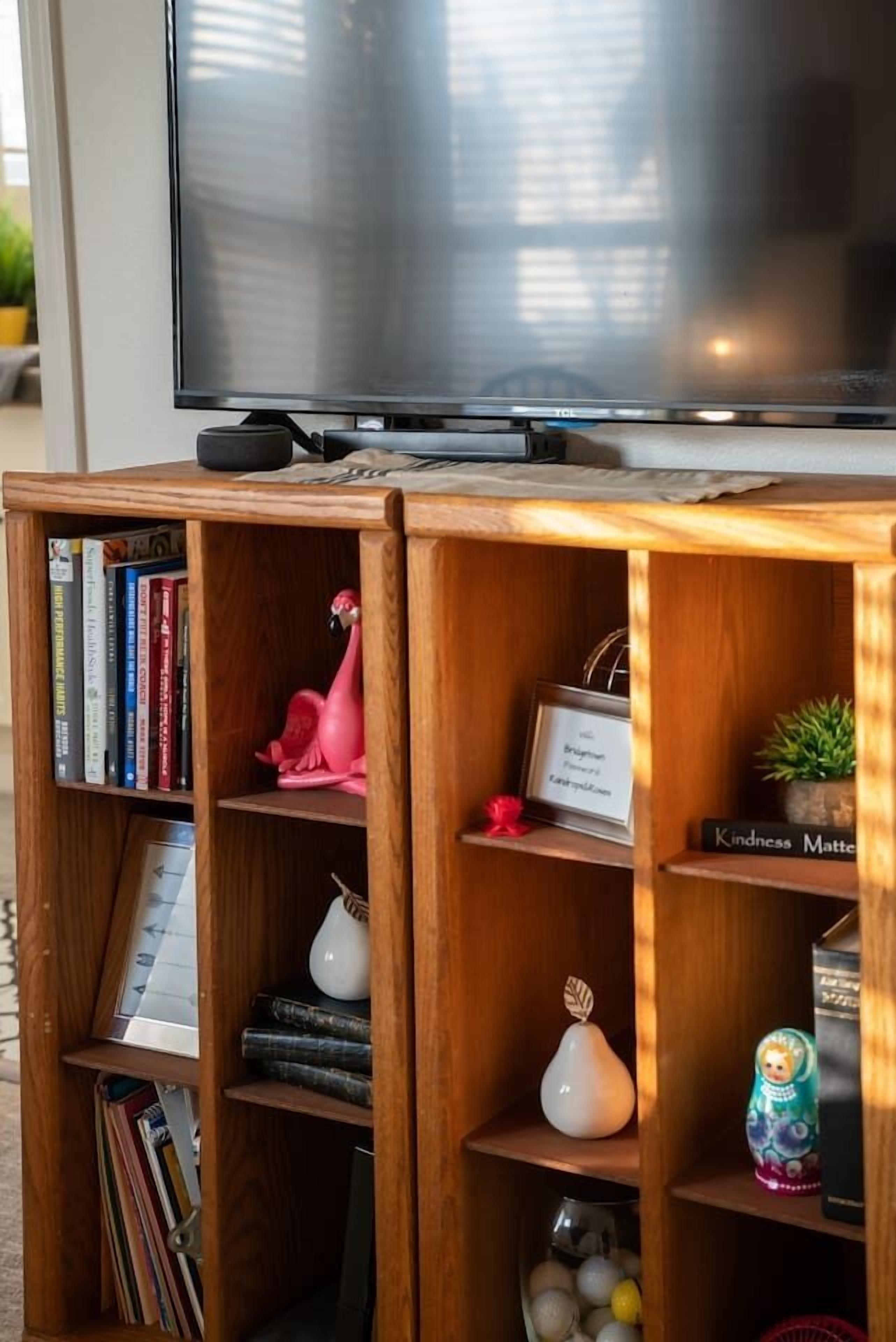 A wooden entertainment unit with a flat-screen TV, books, decorative items, and a small plant.