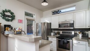 A modern kitchen with white cabinets, stainless steel appliances, a coffee bar, and an exit sign. - Book NOW for Summer Fun! - Perfect for family! - Fully Loaded! - Fire Pit! (Portland)