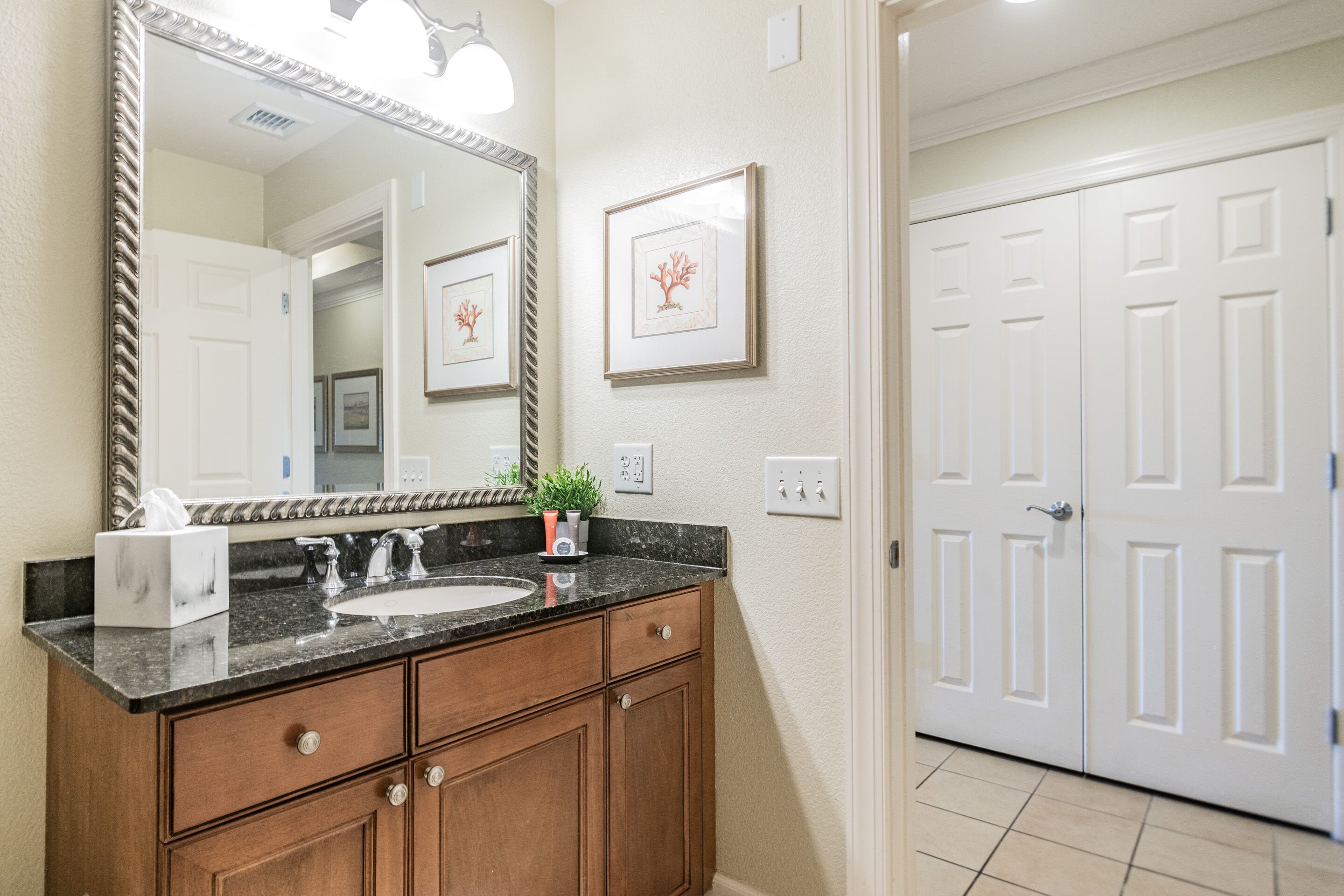 A bathroom with a large mirror, a sink, wooden cabinets, and a framed picture on the wall.