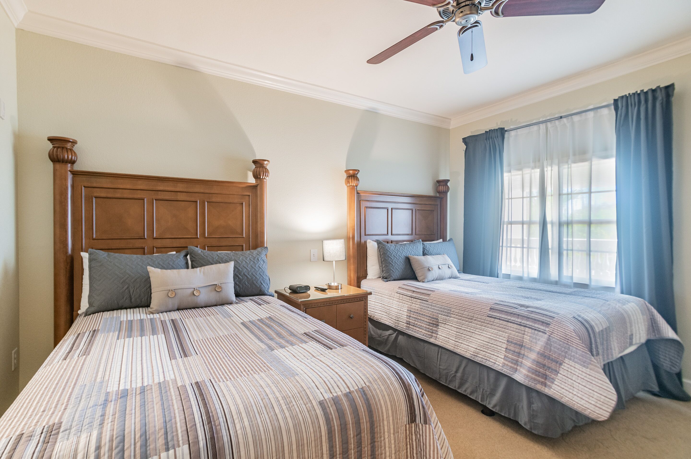 Une chambre avec deux lits, un ventilateur de plafond et une fenêtre avec des rideaux.