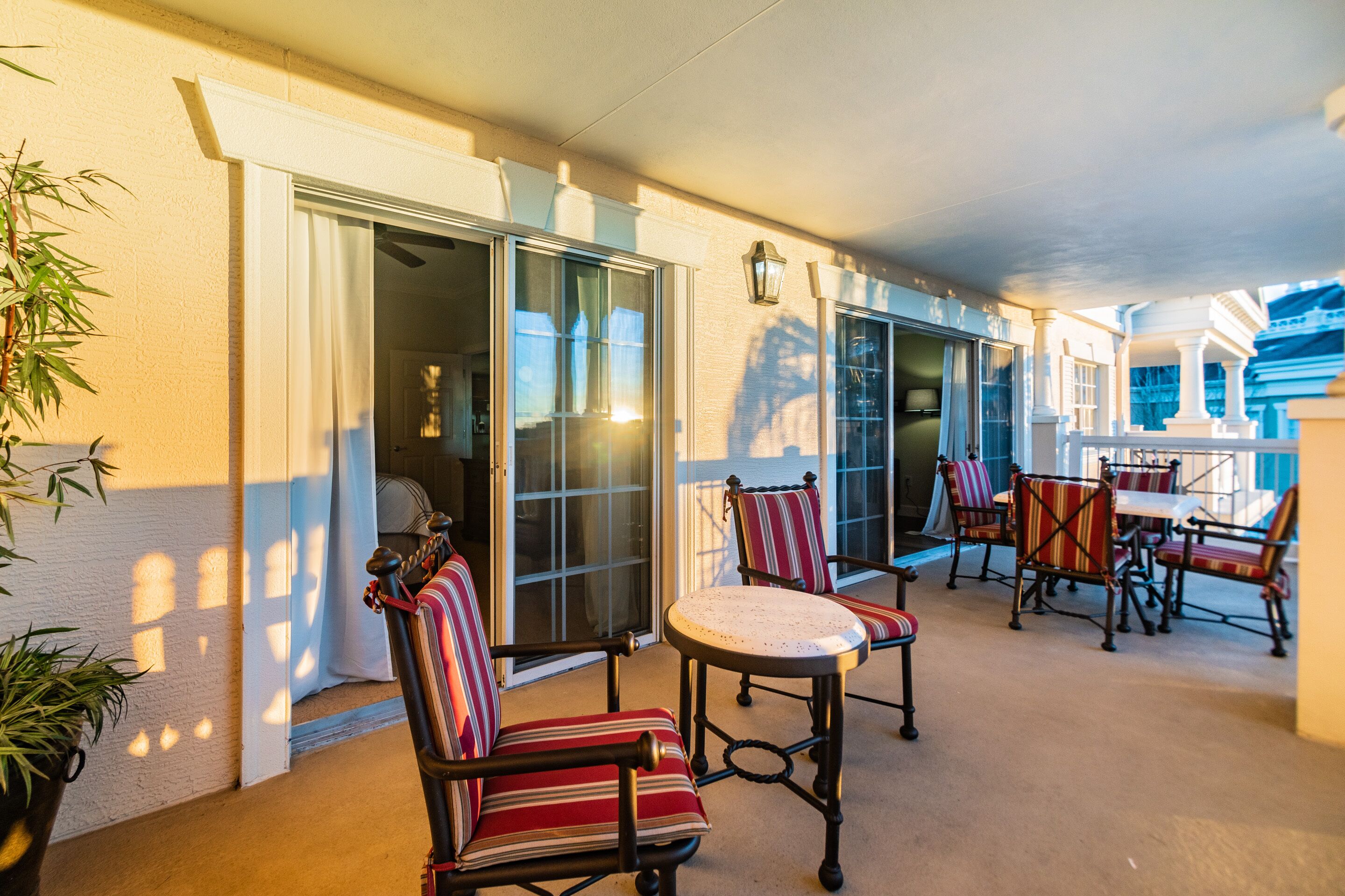 A covered patio with chairs and tables, a sliding glass door, and a potted plant.