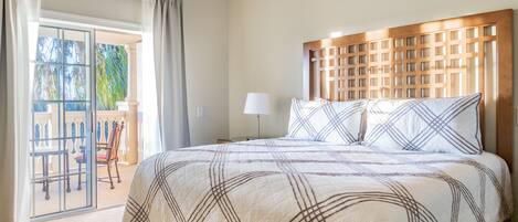 A hotel room with a large bed, a wooden headboard, a balcony with a view, and a sliding glass door.