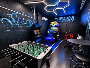 A gaming room with a foosball table, racing game machines, and a neon sign.
